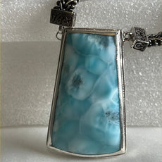 The close up view of the front of Larimar stone of the necklace. The necklace has thick sterling silver chain. A little part of the chain is visible. White background. 